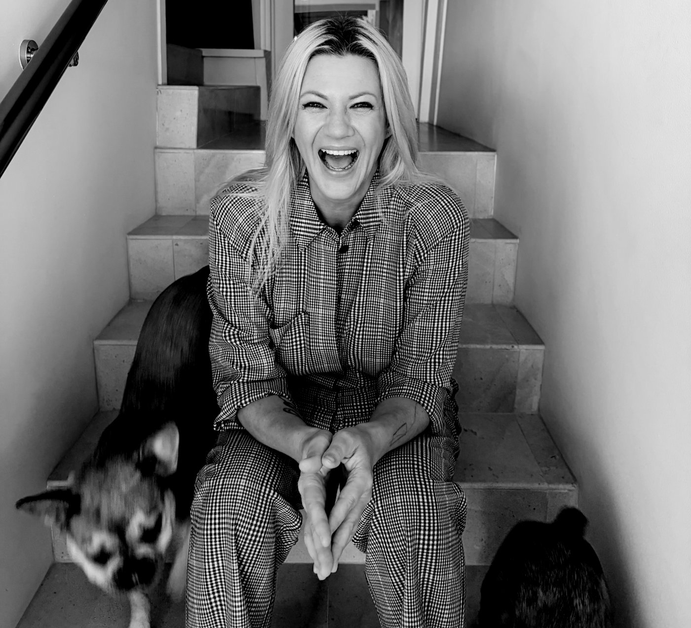 Rachel Airth laughing on the stairs with her dogs Flora and Fern